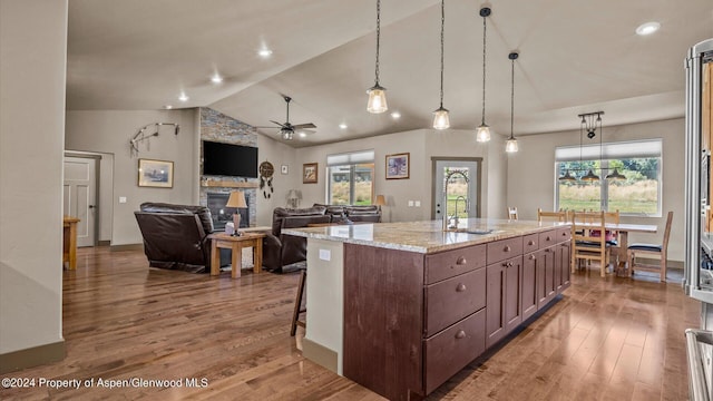 kitchen with light stone counters, ceiling fan, pendant lighting, a center island with sink, and lofted ceiling