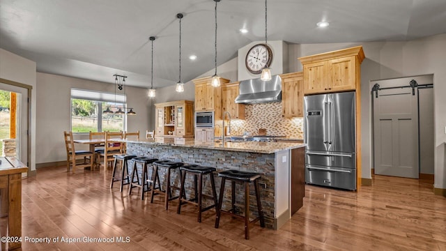 kitchen featuring light brown cabinets, a barn door, pendant lighting, vaulted ceiling, and appliances with stainless steel finishes