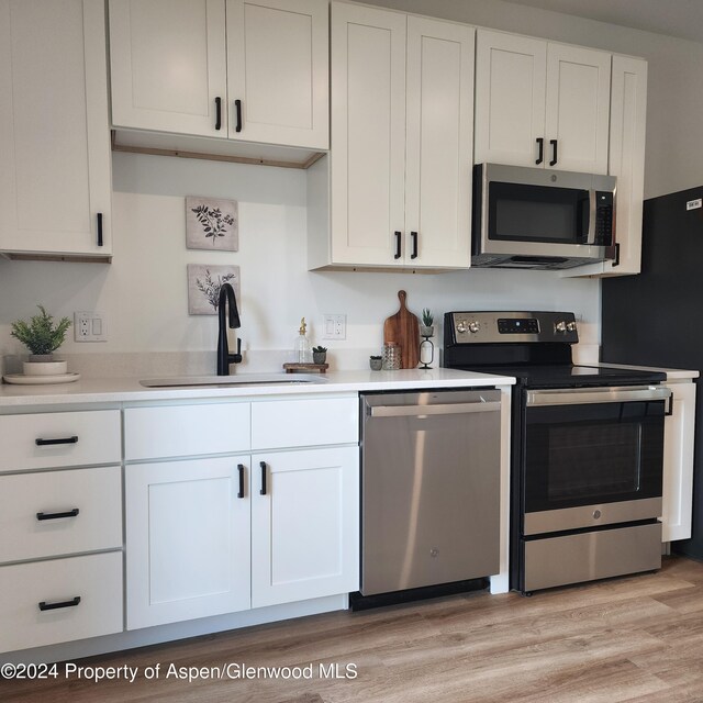 kitchen with white cabinetry, sink, stainless steel appliances, and light hardwood / wood-style floors