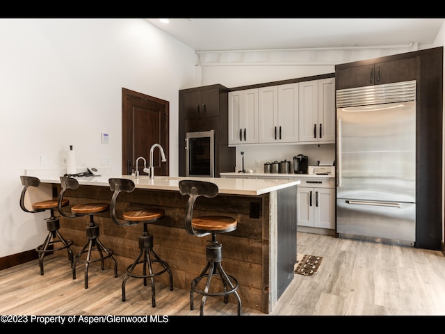 kitchen with stainless steel built in fridge, white cabinetry, a breakfast bar area, and light hardwood / wood-style flooring