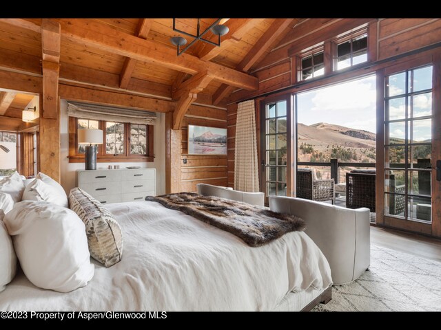 bedroom with lofted ceiling with beams, a mountain view, wooden walls, wood ceiling, and light wood-type flooring