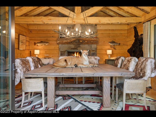 dining area featuring vaulted ceiling with beams, a stone fireplace, wood ceiling, and an inviting chandelier