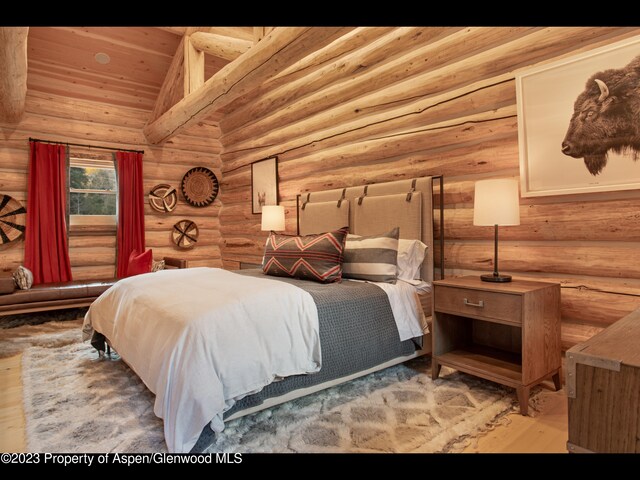 bedroom with hardwood / wood-style floors, high vaulted ceiling, and log walls