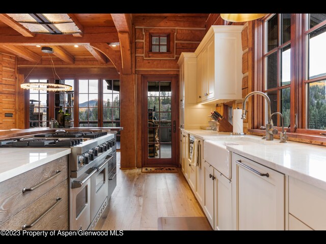 kitchen with beamed ceiling, wood walls, light hardwood / wood-style floors, range with two ovens, and white cabinets