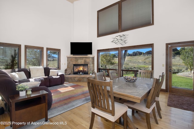 dining room with light hardwood / wood-style floors, a high ceiling, and a stone fireplace