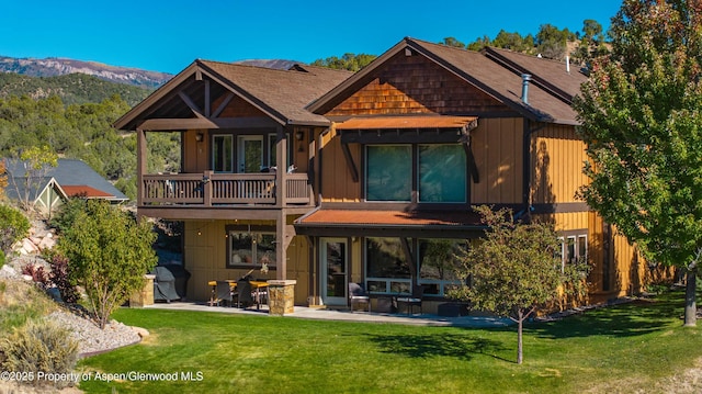 back of property with a balcony, a patio area, a mountain view, and a lawn