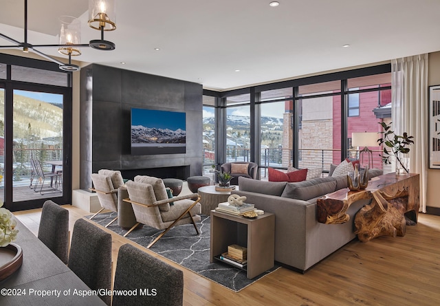 living room with a tiled fireplace, a wall of windows, a notable chandelier, and hardwood / wood-style flooring