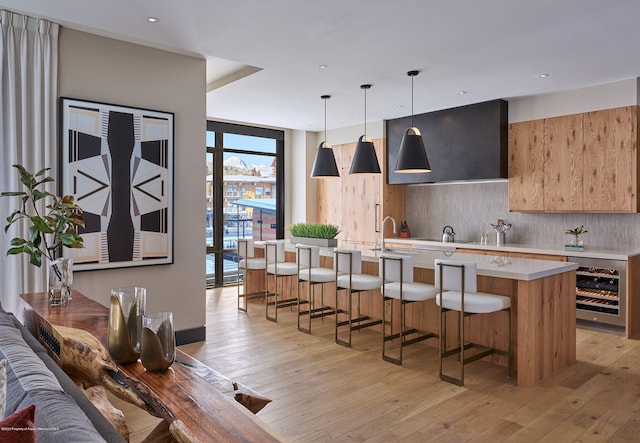 kitchen featuring pendant lighting, backsplash, light hardwood / wood-style flooring, a breakfast bar area, and beverage cooler