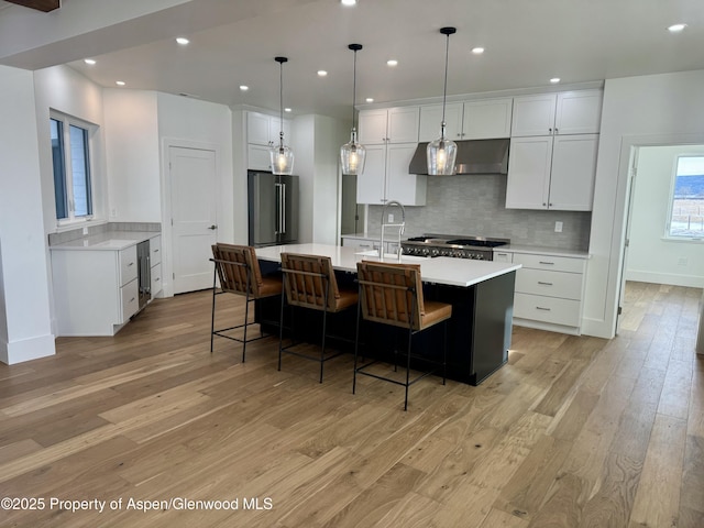 kitchen with white cabinetry, sink, backsplash, an island with sink, and light wood-type flooring