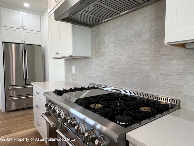 kitchen featuring tasteful backsplash, high end appliances, wall chimney range hood, light hardwood / wood-style flooring, and white cabinetry