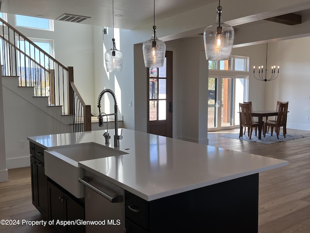 kitchen featuring sink, an inviting chandelier, an island with sink, decorative light fixtures, and light wood-type flooring