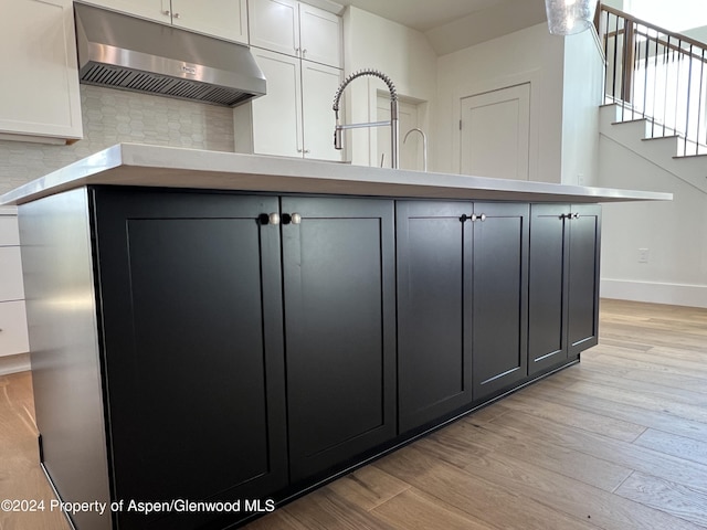 kitchen featuring white cabinets, a center island with sink, sink, decorative backsplash, and light wood-type flooring