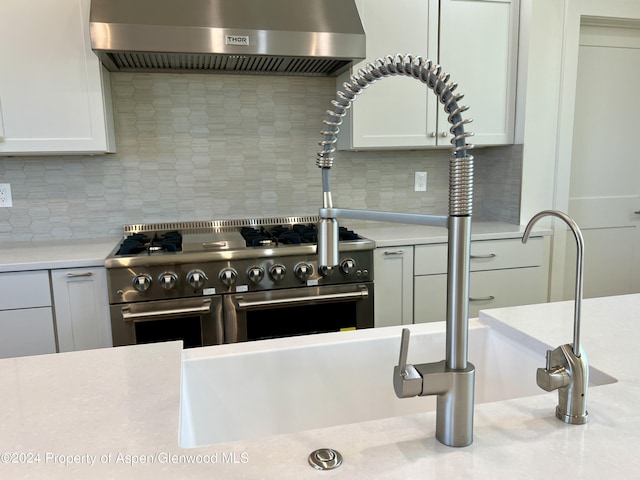 kitchen with white cabinetry, wall chimney range hood, high end stainless steel range oven, and tasteful backsplash