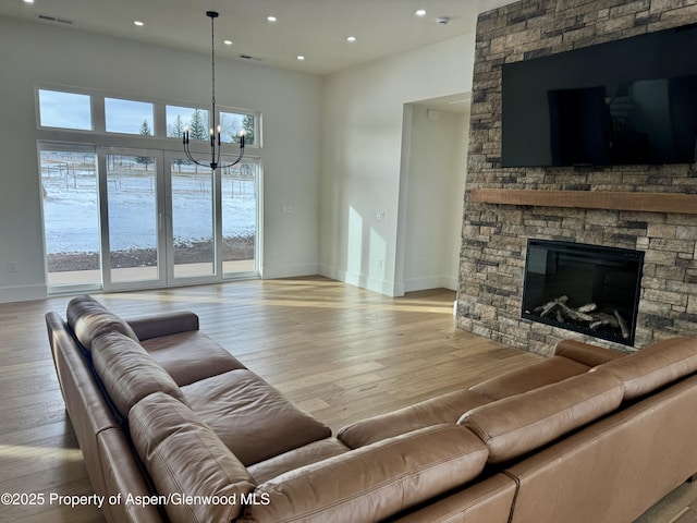 living room featuring a chandelier, light wood-type flooring, a stone fireplace, and plenty of natural light