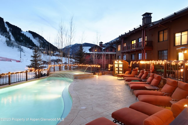 snow covered pool with pool water feature, a mountain view, and a patio