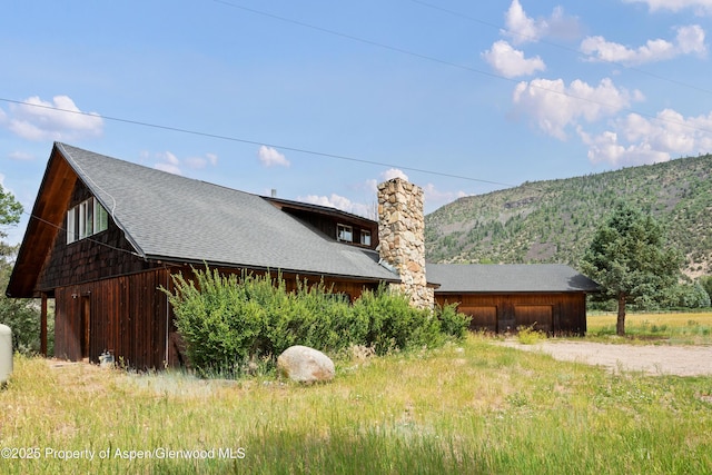 176 Letey Ln, Woody Creek, CO 81656 - view of side of property with driveway, a chimney, a shingled roof, a mountain view, and a detached garage