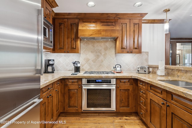 kitchen with backsplash, stainless steel appliances, decorative light fixtures, and light hardwood / wood-style floors