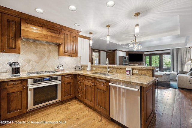 kitchen with kitchen peninsula, tasteful backsplash, stainless steel appliances, sink, and decorative light fixtures