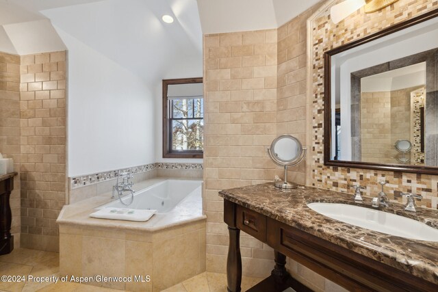 bathroom with tile patterned flooring, vanity, tile walls, and tiled bath