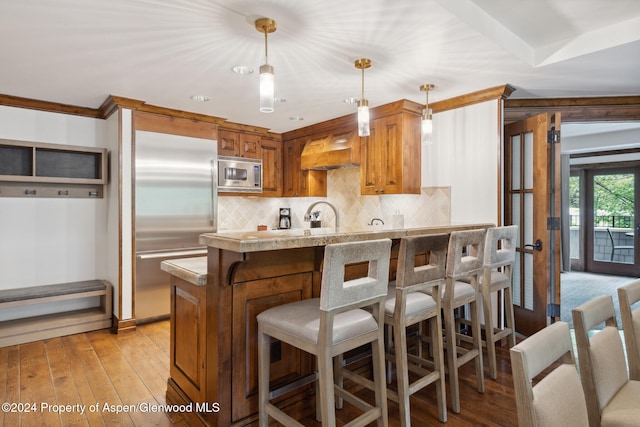 kitchen featuring premium range hood, built in appliances, kitchen peninsula, pendant lighting, and decorative backsplash