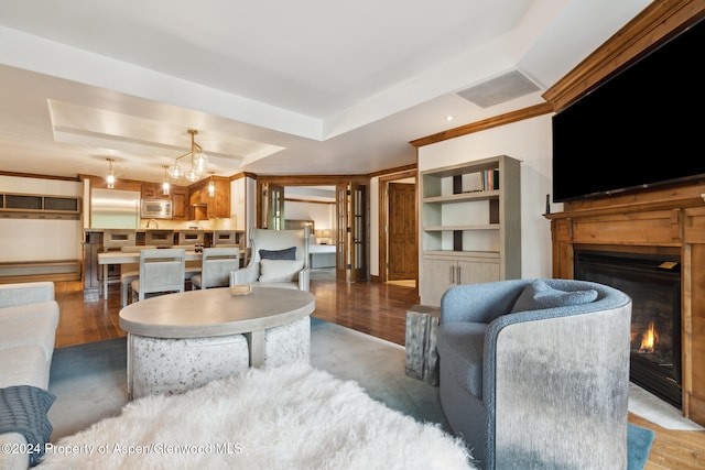 living room featuring light hardwood / wood-style flooring, built in features, a tray ceiling, and a notable chandelier