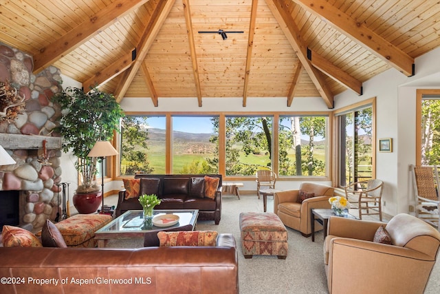 sunroom / solarium with vaulted ceiling with beams, a stone fireplace, a mountain view, and wooden ceiling