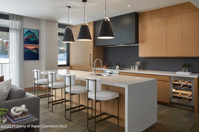 kitchen with sink, tasteful backsplash, wine cooler, decorative light fixtures, and a kitchen island with sink