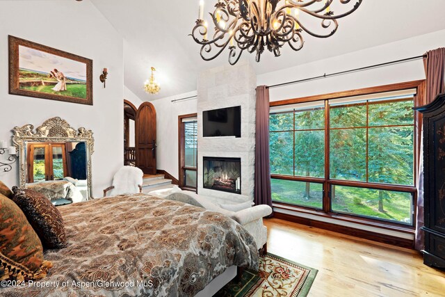 bedroom with a fireplace, light hardwood / wood-style floors, vaulted ceiling, and a notable chandelier