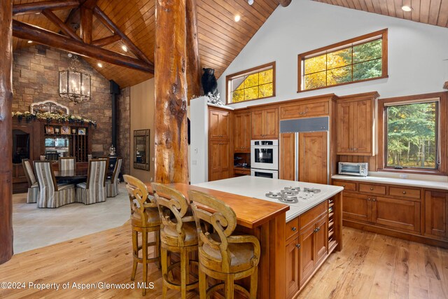 kitchen with a center island, a wood stove, high vaulted ceiling, paneled refrigerator, and light wood-type flooring