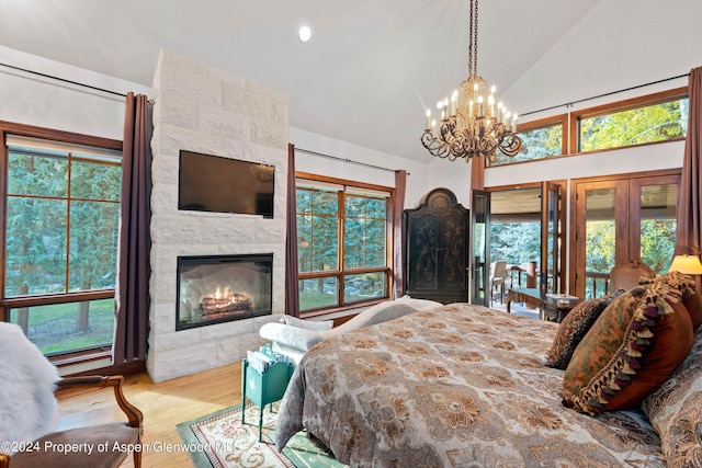 bedroom with hardwood / wood-style floors, high vaulted ceiling, french doors, a notable chandelier, and a tiled fireplace