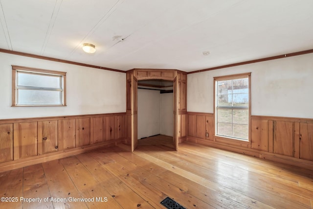 unfurnished bedroom with wooden walls, light wood-style floors, a closet, crown molding, and wainscoting