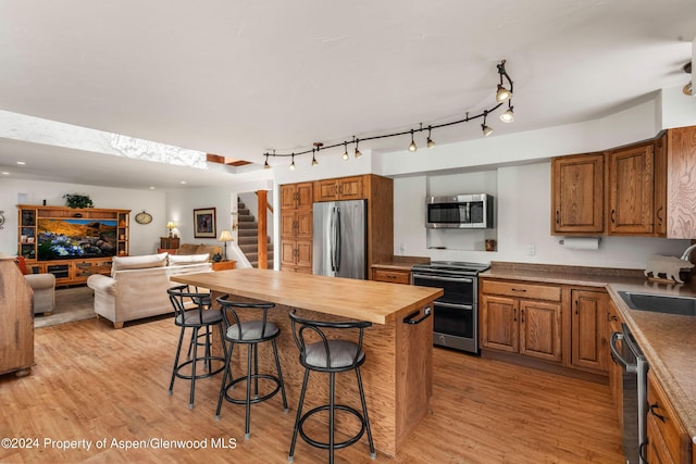 kitchen featuring appliances with stainless steel finishes, sink, light hardwood / wood-style flooring, butcher block counters, and a breakfast bar area