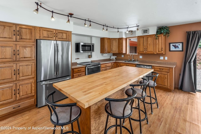 kitchen featuring a kitchen breakfast bar, sink, light hardwood / wood-style flooring, appliances with stainless steel finishes, and butcher block counters