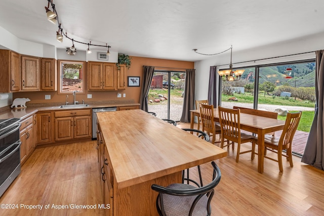 kitchen featuring wooden counters, sink, hanging light fixtures, light hardwood / wood-style flooring, and stainless steel appliances