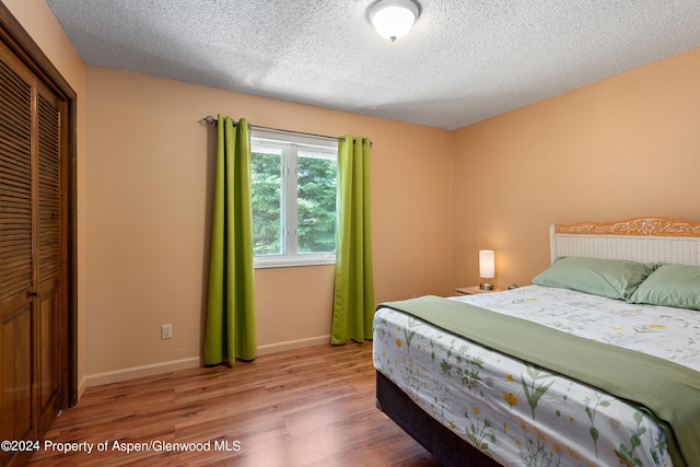 bedroom with a closet, light hardwood / wood-style floors, and a textured ceiling