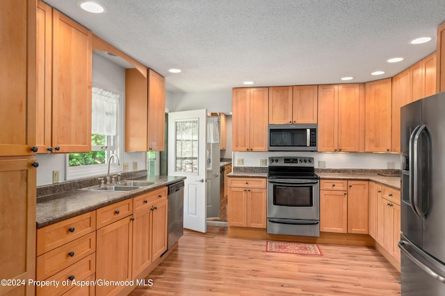 kitchen featuring appliances with stainless steel finishes, a textured ceiling, light hardwood / wood-style floors, and sink