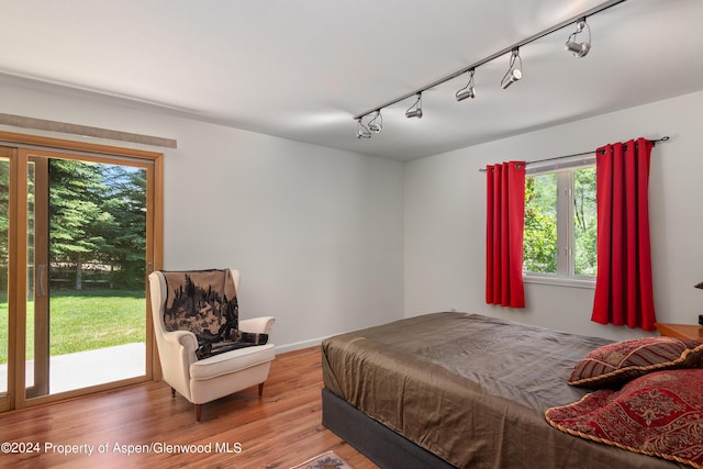 bedroom with access to outside, rail lighting, and hardwood / wood-style flooring