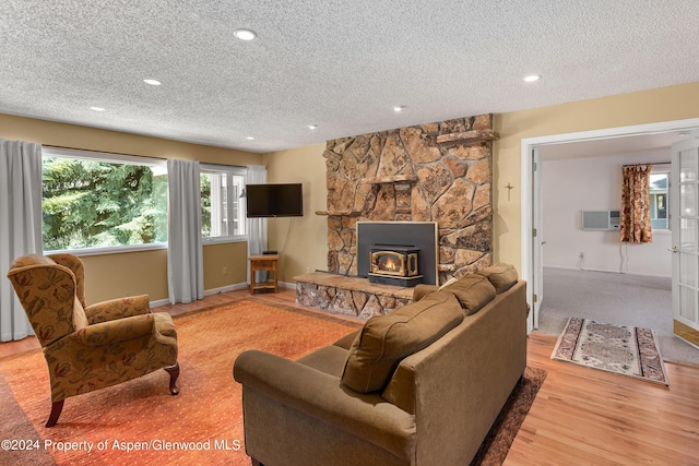 living room featuring a wood stove, a wall mounted AC, a textured ceiling, and light wood-type flooring