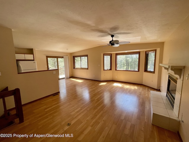 6616 High Dr, Morrison, CO 80465 - unfurnished living room featuring ceiling fan, vaulted ceiling, light wood-style flooring, a tiled fireplace, and a textured ceiling