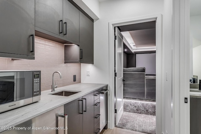 kitchen featuring gray cabinets, light stone counters, sink, and decorative backsplash