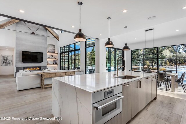 kitchen featuring a large fireplace, sink, hanging light fixtures, a spacious island, and light hardwood / wood-style floors