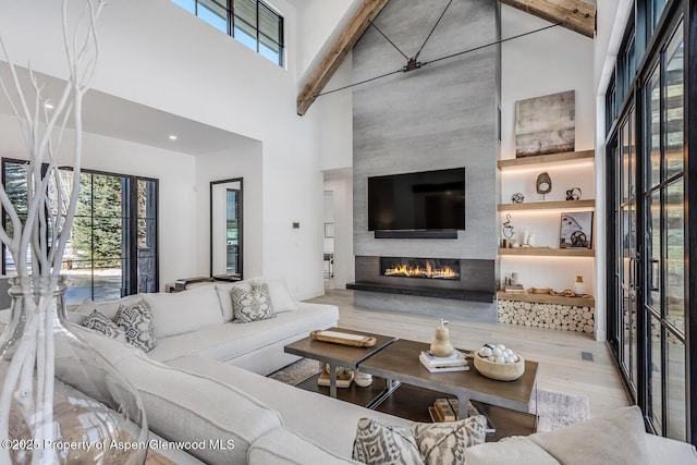 living room with a fireplace, beamed ceiling, light hardwood / wood-style floors, and a high ceiling