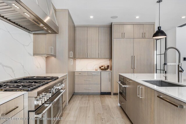 kitchen featuring light brown cabinets, wall chimney range hood, sink, high end stainless steel range oven, and hanging light fixtures