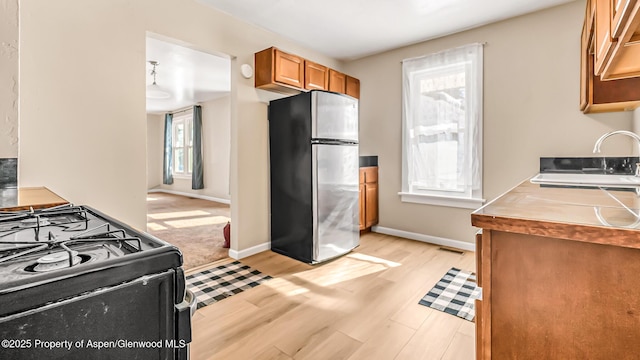 kitchen featuring sink, gas stove, stainless steel fridge, and light hardwood / wood-style floors