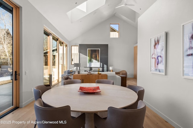 dining space with a skylight, high vaulted ceiling, and light wood-type flooring