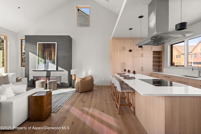 kitchen featuring sink, hanging light fixtures, black electric cooktop, island range hood, and light brown cabinetry