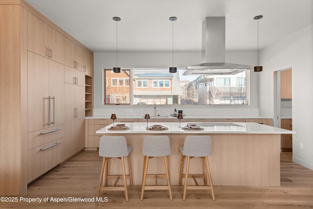 kitchen featuring light brown cabinets, hanging light fixtures, island exhaust hood, a center island with sink, and light hardwood / wood-style flooring