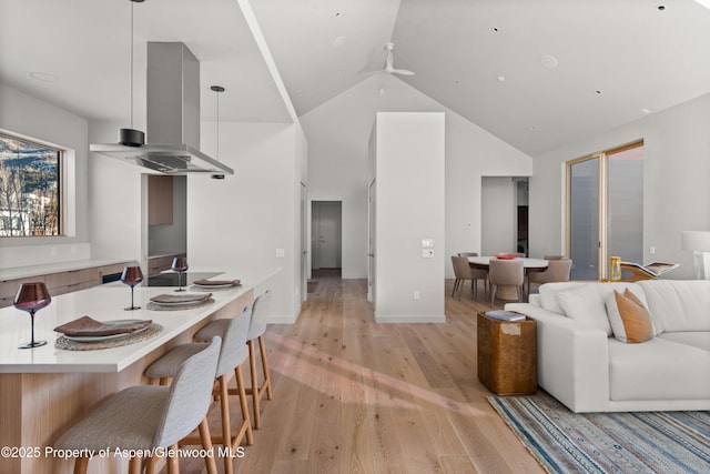 kitchen with island range hood, high vaulted ceiling, decorative light fixtures, ceiling fan, and light wood-type flooring