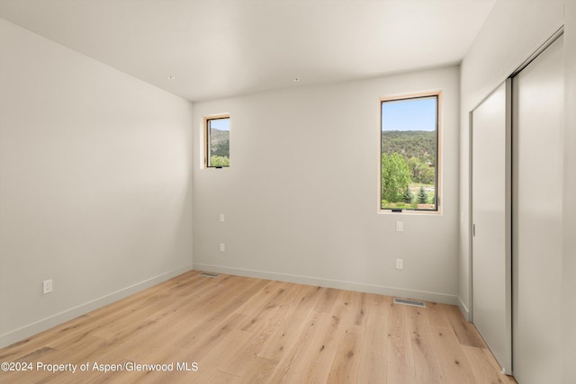 unfurnished bedroom featuring a closet, multiple windows, and light wood-type flooring