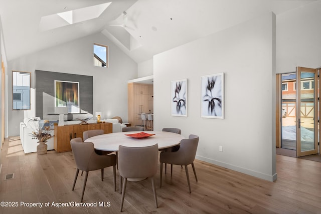 dining room with high vaulted ceiling, a skylight, light hardwood / wood-style floors, and ceiling fan